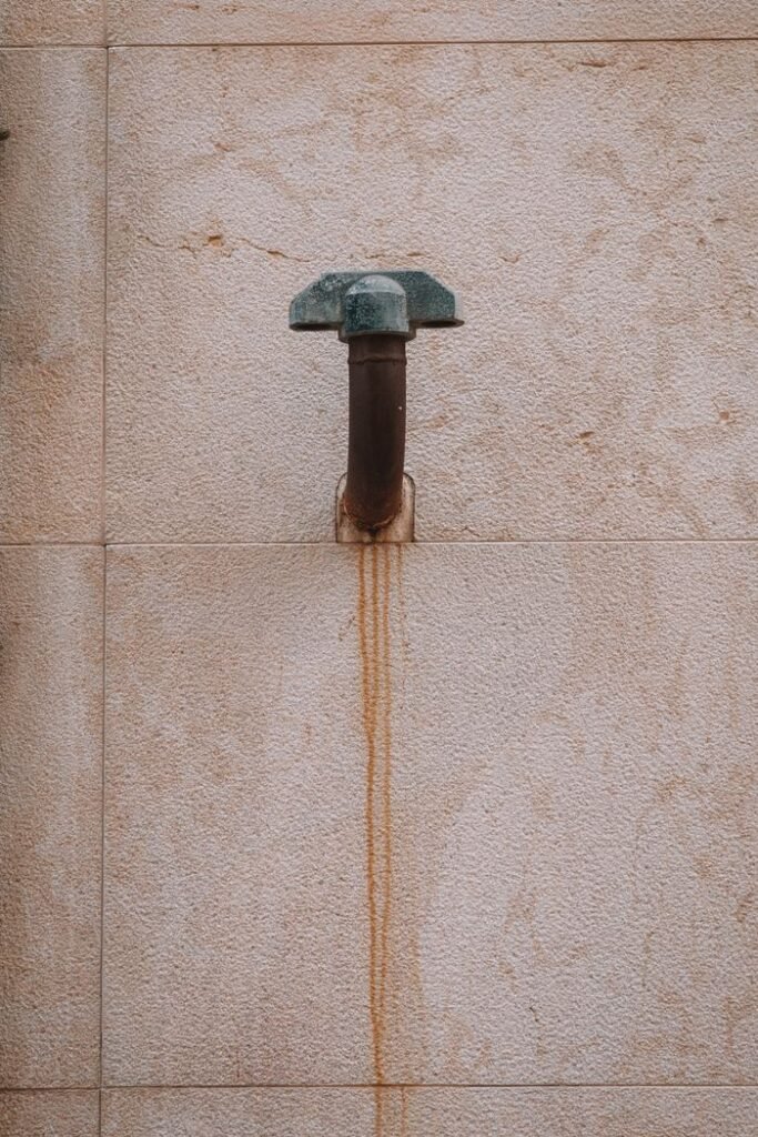 An aged and rusty metal pipe attached to a textured wall in Valencia, Spain.